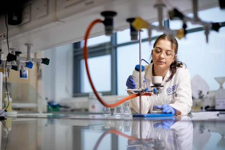 Female student sat working with chemistry equipment in a lab