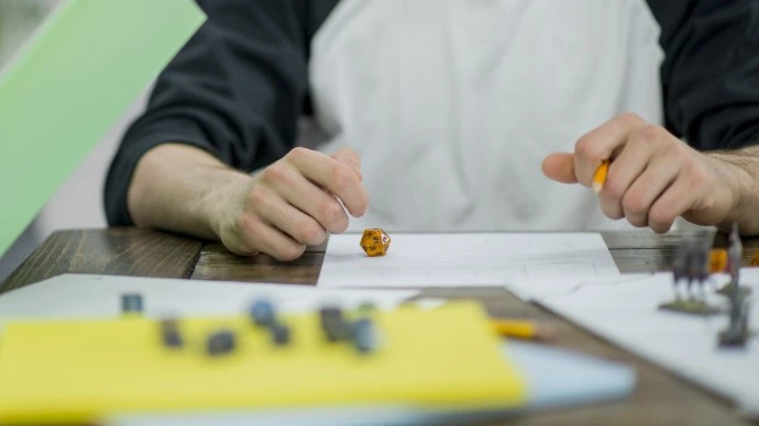 A tabletop role playing game set up with dice and the hands of a player in the background