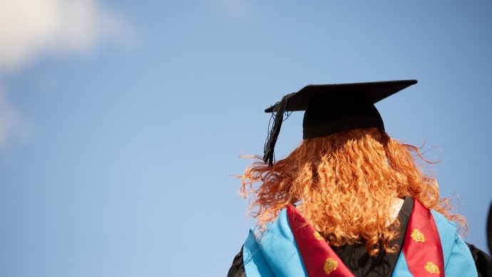 Graduate in gown and hat looking out to the blue sky 
