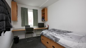 A university accommodation room, featuring a single bed and a desk.