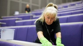 A cleaner wiping down desks in a lecture theatre