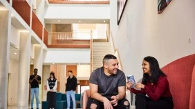 Two students chatting and laughing on a lobby area sofa