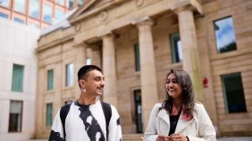 Two students engaged in conversation in front of old art school building