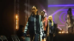 Group of fashion models walking down a runway in a modern, industrial setting, with a large screen backdrop