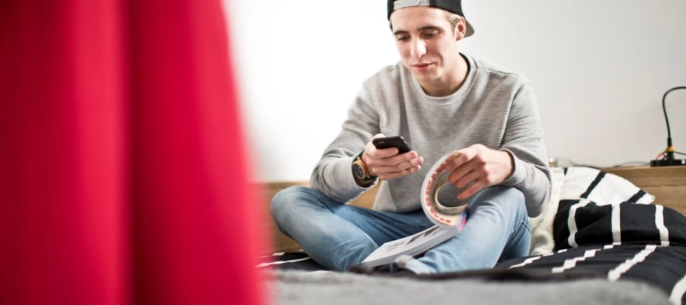 Student checking his phone while reading on the bed